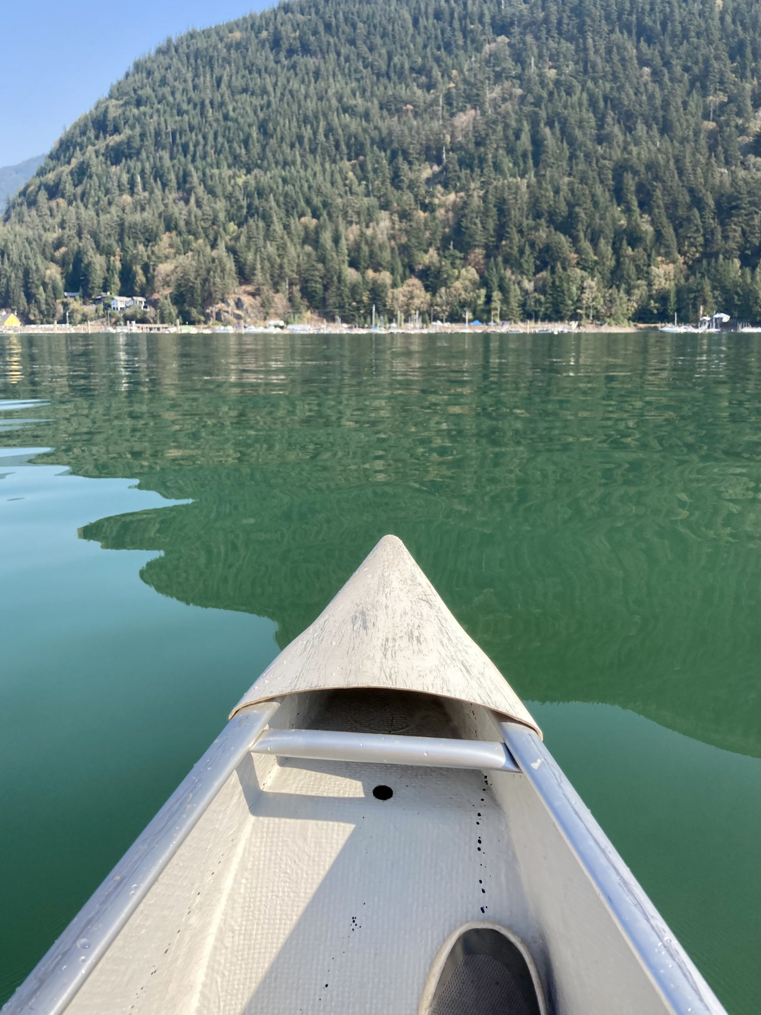 The view of an emerald-green lake from the front of a white canoe, with forested mountains past the distant shore