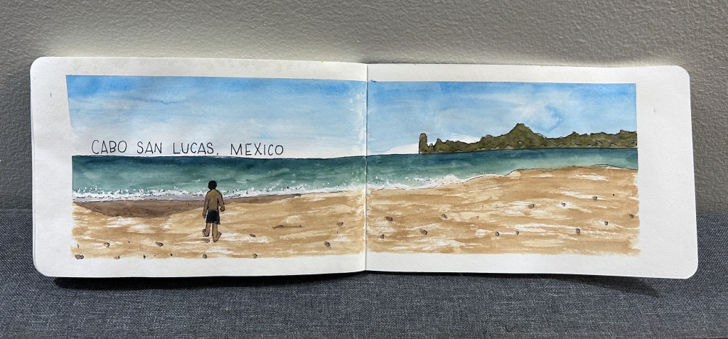 A two-page sketchbook spread with a watercolor painting of a wide beach with waves crashing and a rock formation at the horizon